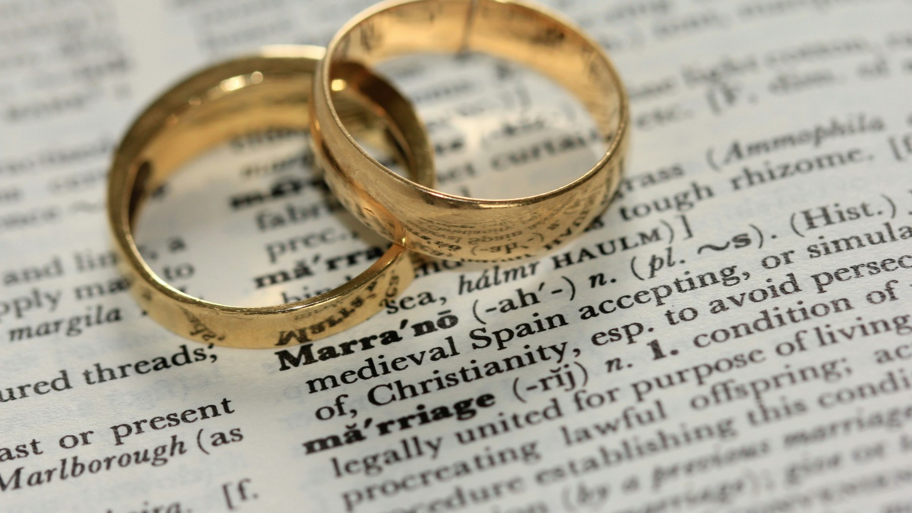Two gold wedding rings resting on a dictionary page open at the word marriage.